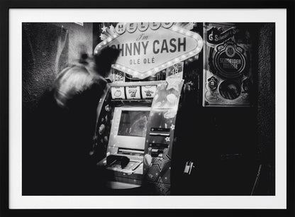 A grainy, black and white photograph of a person blurred by motion standing in front of a Johnny Cash themed slot machine. A lit marquee sign above the machine reads "HELLO I'm JOHNNY CASH OLÉ OLÉ". The setting appears to be a dark bar or casino. Wall Art