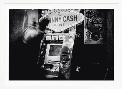 A grainy, black and white photograph of a person blurred by motion standing in front of a Johnny Cash themed slot machine. A lit marquee sign above the machine reads "HELLO I'm JOHNNY CASH OLÉ OLÉ". The setting appears to be a dark bar or casino. Wall Art