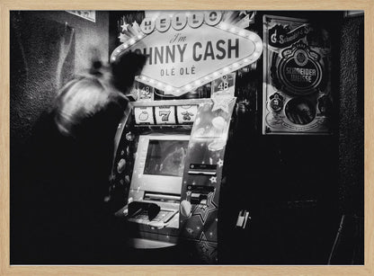 A grainy, black and white photograph of a person blurred by motion standing in front of a Johnny Cash themed slot machine. A lit marquee sign above the machine reads "HELLO I'm JOHNNY CASH OLÉ OLÉ". The setting appears to be a dark bar or casino. Wall Art