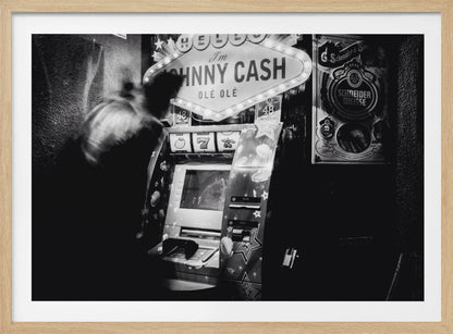 A grainy, black and white photograph of a person blurred by motion standing in front of a Johnny Cash themed slot machine. A lit marquee sign above the machine reads "HELLO I'm JOHNNY CASH OLÉ OLÉ". The setting appears to be a dark bar or casino. Wall Art