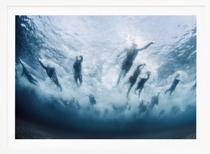 An underwater photograph looking up at a group of swimmers competing in a race. Their bodies are silhouetted against the bright surface of the turbulent blue water, captured mid-motion amidst a flurry of bubbles and foam. Print