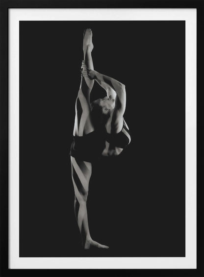 A dramatic black and white studio photograph of a female dancer performing a standing split. She balances on one leg while holding the other leg straight up vertically next to her head, arching her back and looking upwards. The strong side lighting creates a chiaroscuro effect, highlighting her musculature and form against a solid black background. Print
