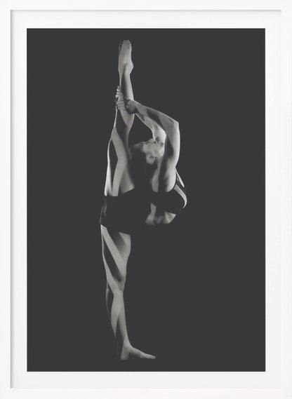 A dramatic black and white studio photograph of a female dancer performing a standing split. She balances on one leg while holding the other leg straight up vertically next to her head, arching her back and looking upwards. The strong side lighting creates a chiaroscuro effect, highlighting her musculature and form against a solid black background. Print