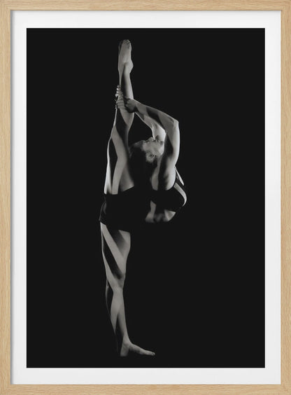 A dramatic black and white studio photograph of a female dancer performing a standing split. She balances on one leg while holding the other leg straight up vertically next to her head, arching her back and looking upwards. The strong side lighting creates a chiaroscuro effect, highlighting her musculature and form against a solid black background. Print