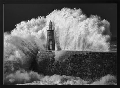 A dramatic black and white photograph of a massive wave crashing against a stone pier and a small lighthouse. The white foam of the wave towers over the structure, creating a powerful and dynamic scene against a dark sky, all enclosed in a silver frame. Poster