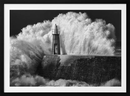 A dramatic black and white photograph of a massive wave crashing against a stone pier and a small lighthouse. The white foam of the wave towers over the structure, creating a powerful and dynamic scene against a dark sky, all enclosed in a silver frame. Poster