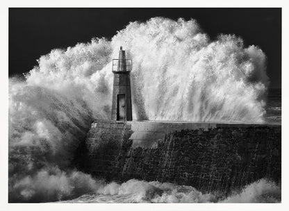 A dramatic black and white photograph of a massive wave crashing against a stone pier and a small lighthouse. The white foam of the wave towers over the structure, creating a powerful and dynamic scene against a dark sky, all enclosed in a silver frame. Poster