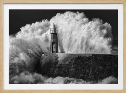 A dramatic black and white photograph of a massive wave crashing against a stone pier and a small lighthouse. The white foam of the wave towers over the structure, creating a powerful and dynamic scene against a dark sky, all enclosed in a silver frame. Poster