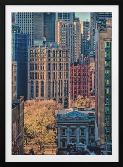 A high-angle view of a dense city skyline featuring a mix of old and new architectural styles. Golden light illuminates the autumn foliage of a park and the facades of several buildings, creating a warm contrast with the cool blue tones of the skyscrapers in the background. Decor