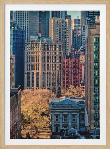 A high-angle view of a dense city skyline featuring a mix of old and new architectural styles. Golden light illuminates the autumn foliage of a park and the facades of several buildings, creating a warm contrast with the cool blue tones of the skyscrapers in the background. Decor