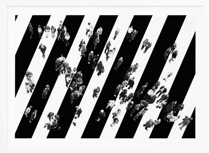 A striking black and white aerial photograph of dozens of people walking across a large, diagonally striped crosswalk. The high-contrast, graphic pattern of black and white stripes dominates the scene, with the small figures of pedestrians scattered across it, creating a sense of movement and urban anonymity. The image is presented within a simple silver frame. Print
