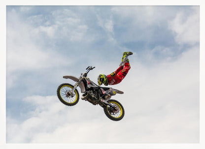 A motocross rider in red and yellow gear performs a high-flying stunt, arching their back while upside down in the air next to their dirt bike, set against a backdrop of a blue sky with white clouds and enclosed in a silver frame. Poster