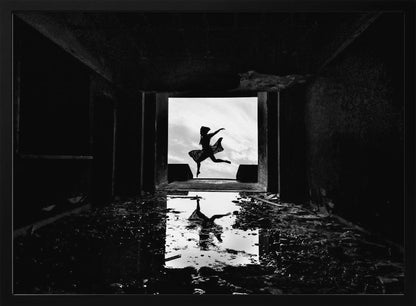 A dramatic black and white photo of a silhouetted dancer leaping in a bright doorway, viewed from inside a dark, derelict building. The dancer's reflection is captured in a puddle on the rubble-strewn floor. Poster
