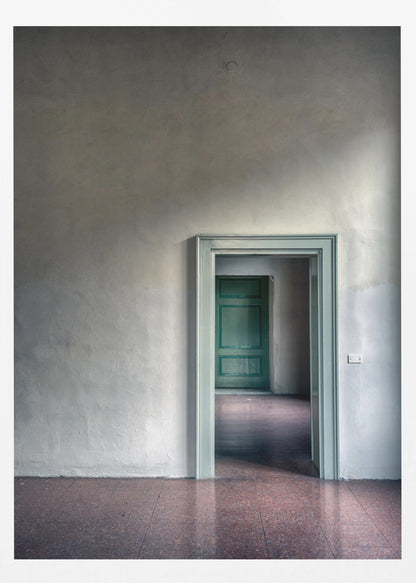 A minimalist photograph of a room with grey, textured walls and a reddish-brown floor, focusing on an open, light green doorway that reveals another room with a closed, darker green door, creating a sense of depth and perspective. Wall Art