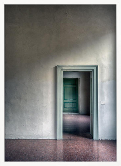 A minimalist photograph of a room with grey, textured walls and a reddish-brown floor, focusing on an open, light green doorway that reveals another room with a closed, darker green door, creating a sense of depth and perspective. Wall Art