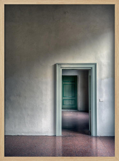 A minimalist photograph of a room with grey, textured walls and a reddish-brown floor, focusing on an open, light green doorway that reveals another room with a closed, darker green door, creating a sense of depth and perspective. Wall Art