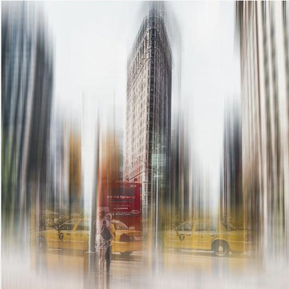 An artistic photograph of New York City's Flatiron Building in a light wood frame. The image has a strong vertical motion blur effect, creating streaks of yellow from taxi cabs and gray from the surrounding architecture, capturing the bustling energy of the city. Poster