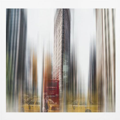 An artistic photograph of New York City's Flatiron Building in a light wood frame. The image has a strong vertical motion blur effect, creating streaks of yellow from taxi cabs and gray from the surrounding architecture, capturing the bustling energy of the city. Poster