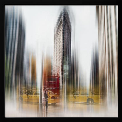 An artistic photograph of New York City's Flatiron Building in a light wood frame. The image has a strong vertical motion blur effect, creating streaks of yellow from taxi cabs and gray from the surrounding architecture, capturing the bustling energy of the city. Poster