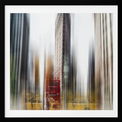 An artistic photograph of New York City's Flatiron Building in a light wood frame. The image has a strong vertical motion blur effect, creating streaks of yellow from taxi cabs and gray from the surrounding architecture, capturing the bustling energy of the city. Poster