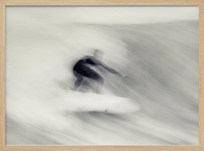 An artistic black and white photograph using motion blur to capture a surfer in a dynamic, fluid pose on a wave. The slow shutter speed creates a sense of speed and abstract movement, with the surfer's dark wetsuit contrasting against the white, streaked water. The image is presented in a silver frame. Decor