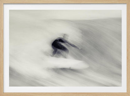 An artistic black and white photograph using motion blur to capture a surfer in a dynamic, fluid pose on a wave. The slow shutter speed creates a sense of speed and abstract movement, with the surfer's dark wetsuit contrasting against the white, streaked water. The image is presented in a silver frame. Decor