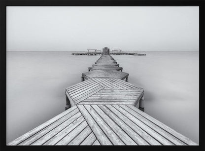 A framed, black and white photograph capturing a long wooden pier from a first-person perspective. The pier, constructed from a series of hexagonal platforms, stretches out into a calm, placid body of water that disappears into a foggy horizon, creating a serene and minimalist scene. Print