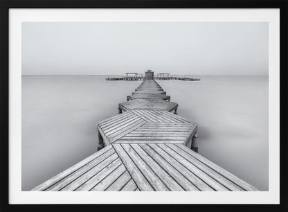 A framed, black and white photograph capturing a long wooden pier from a first-person perspective. The pier, constructed from a series of hexagonal platforms, stretches out into a calm, placid body of water that disappears into a foggy horizon, creating a serene and minimalist scene. Print