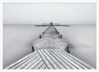 A framed, black and white photograph capturing a long wooden pier from a first-person perspective. The pier, constructed from a series of hexagonal platforms, stretches out into a calm, placid body of water that disappears into a foggy horizon, creating a serene and minimalist scene. Print