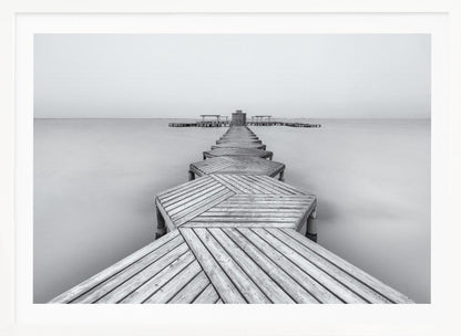 A framed, black and white photograph capturing a long wooden pier from a first-person perspective. The pier, constructed from a series of hexagonal platforms, stretches out into a calm, placid body of water that disappears into a foggy horizon, creating a serene and minimalist scene. Print