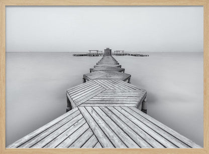 A framed, black and white photograph capturing a long wooden pier from a first-person perspective. The pier, constructed from a series of hexagonal platforms, stretches out into a calm, placid body of water that disappears into a foggy horizon, creating a serene and minimalist scene. Print