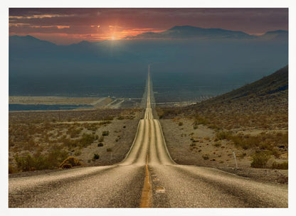 A high-angle view of a long, straight, and hilly road disappearing into the horizon of a vast desert valley at sunset, with mountains in the background under a warm, glowing sky, all enclosed in a silver frame. Poster