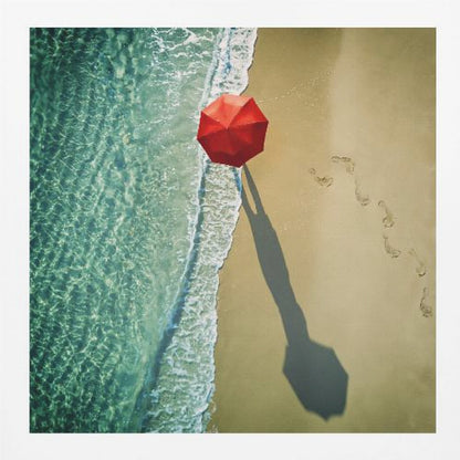An aerial photograph of a serene beach scene, featuring a vibrant red umbrella on the golden sand next to the clear turquoise ocean. Gentle white waves lap the shore, and a long shadow from the umbrella stretches across the sand, where a trail of footprints leads away. Poster