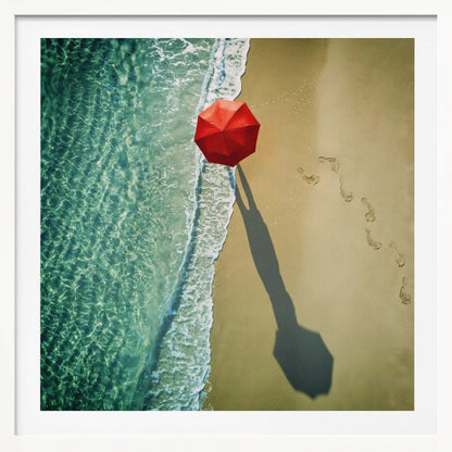 An aerial photograph of a serene beach scene, featuring a vibrant red umbrella on the golden sand next to the clear turquoise ocean. Gentle white waves lap the shore, and a long shadow from the umbrella stretches across the sand, where a trail of footprints leads away. Poster