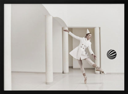 A ballerina dressed in a white quilted coat and a pointed hat dances en pointe in a minimalist white hall with large columns. She gracefully extends her arms, looking towards a black and white striped ball that appears to be floating in mid-air. The scene is presented within a silver picture frame. Wall Art