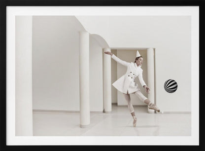 A ballerina dressed in a white quilted coat and a pointed hat dances en pointe in a minimalist white hall with large columns. She gracefully extends her arms, looking towards a black and white striped ball that appears to be floating in mid-air. The scene is presented within a silver picture frame. Wall Art