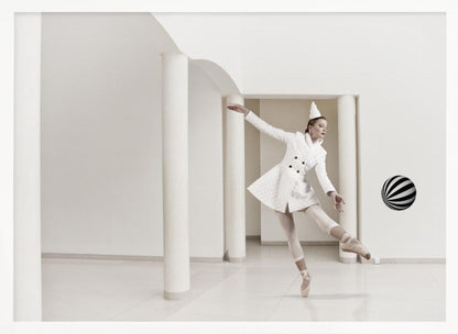A ballerina dressed in a white quilted coat and a pointed hat dances en pointe in a minimalist white hall with large columns. She gracefully extends her arms, looking towards a black and white striped ball that appears to be floating in mid-air. The scene is presented within a silver picture frame. Wall Art