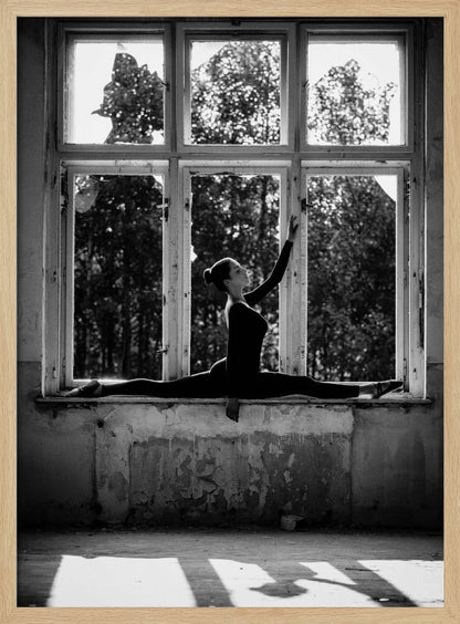 A black and white photograph of a graceful female dancer holding a perfect split on a large, dilapidated windowsill. She is silhouetted against the bright light from the broken window panes, with her arm elegantly raised. The setting is an abandoned room with peeling paint, creating a stark contrast between the dancer's elegance and the decaying environment. Wall Art