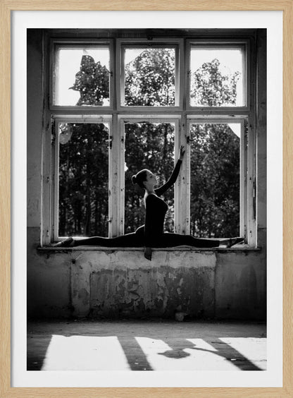 A black and white photograph of a graceful female dancer holding a perfect split on a large, dilapidated windowsill. She is silhouetted against the bright light from the broken window panes, with her arm elegantly raised. The setting is an abandoned room with peeling paint, creating a stark contrast between the dancer's elegance and the decaying environment. Wall Art