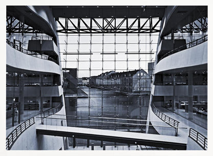 A symmetrical, black and white photograph taken from inside a modern building with curved balconies, looking out through a massive glass wall onto a canal and historic buildings on the opposite bank. A pedestrian bridge crosses the lower part of the frame. Decor