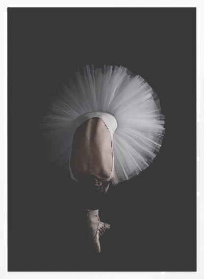 A dramatic photograph of a ballerina against a solid black background. She is bent completely forward, showing her arched back to the camera. Her white tutu fans out in a wide circle around her, and one foot in a pointe shoe is visible beneath her, balanced on its tip. Print