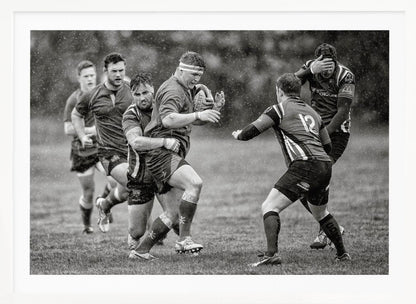 A dynamic black and white photograph of a rugby match being played in the rain. One player charges forward with the ball while an opponent wraps his arms around him in a tackle. Other players are in motion around them, capturing the intensity and physicality of the sport. Decor