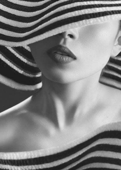 A mysterious black and white close-up portrait of a woman wearing a large, floppy hat with bold black and white stripes. The hat's brim covers her eyes, revealing only her nose, full lips, and chin, creating an elegant and enigmatic look. Decor