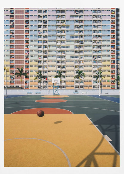 A vibrant photograph of a basketball court with a yellow and green floor, a single basketball is mid-bounce in the foreground. In the background stands the massive, symmetrical Choi Hung Estate apartment building in Hong Kong, famous for its facade of pastel rainbow colors. Palm trees line the space between the court and the building. Print