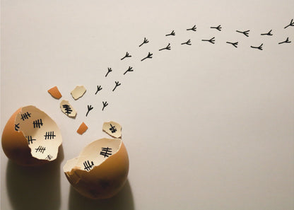 A conceptual art piece showing a broken brown eggshell against a beige background. Inside the shell are black tally marks, as if counting days. A trail of tiny black chicken footprints leads away from the egg, suggesting a chick has finally hatched and escaped after a long wait. Artwork