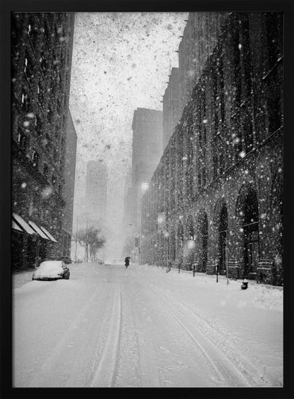 A grainy, black and white photograph captures a deserted city street during a heavy snowstorm. Tall buildings line the street, which is covered in a thick blanket of snow. A single car on the left is almost completely buried, and in the distance, a lone figure walks with an umbrella down the center of the empty road. Poster