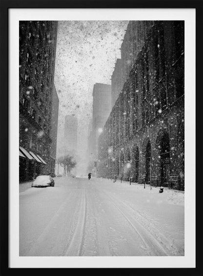A grainy, black and white photograph captures a deserted city street during a heavy snowstorm. Tall buildings line the street, which is covered in a thick blanket of snow. A single car on the left is almost completely buried, and in the distance, a lone figure walks with an umbrella down the center of the empty road. Poster