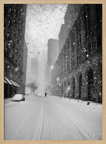 A grainy, black and white photograph captures a deserted city street during a heavy snowstorm. Tall buildings line the street, which is covered in a thick blanket of snow. A single car on the left is almost completely buried, and in the distance, a lone figure walks with an umbrella down the center of the empty road. Poster