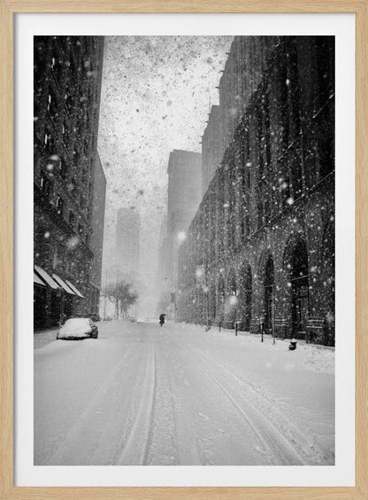 A grainy, black and white photograph captures a deserted city street during a heavy snowstorm. Tall buildings line the street, which is covered in a thick blanket of snow. A single car on the left is almost completely buried, and in the distance, a lone figure walks with an umbrella down the center of the empty road. Poster