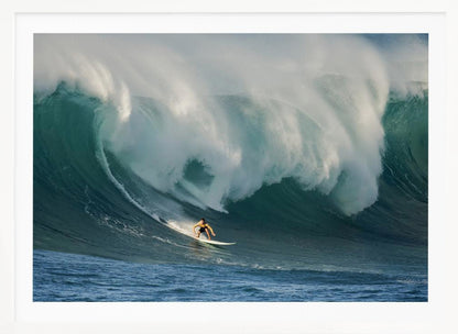 A lone surfer in a yellow shirt rides down the face of an enormous, powerful ocean wave as it crests into white foam, viewed within a silver picture frame. Wall Art